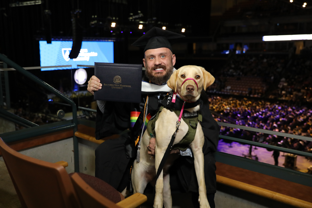 Jereme West, accompanied by his loyal service dog Lillie, holds his diploma at SNHU Commencement.