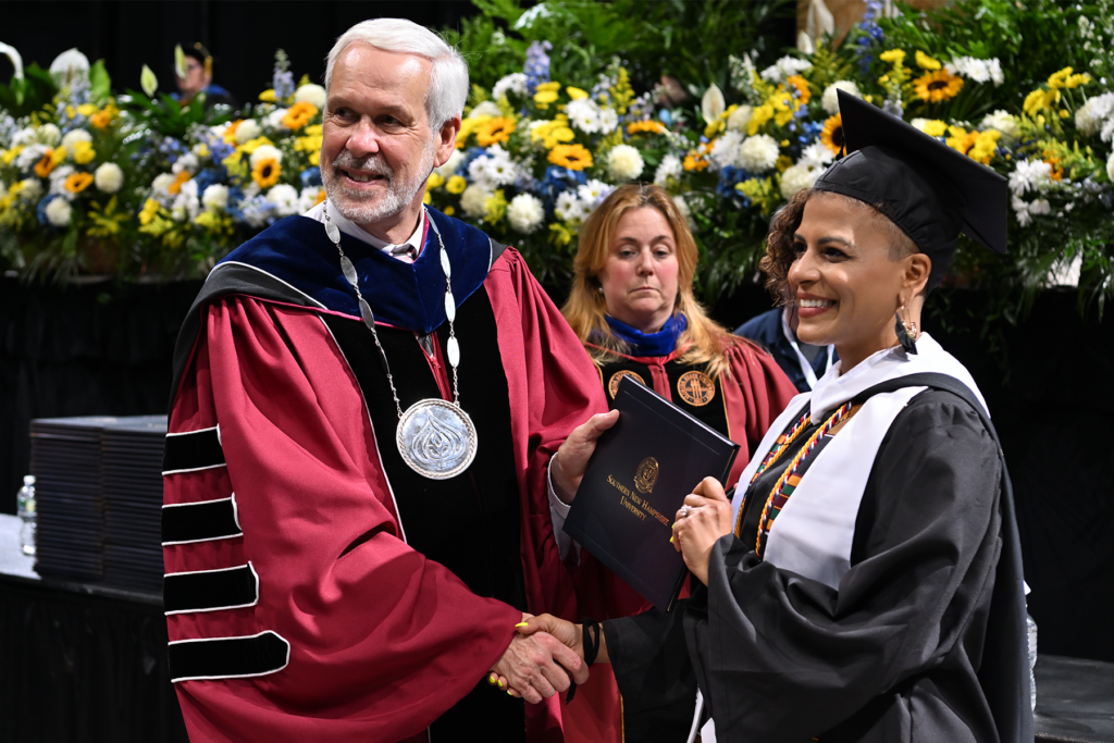 Tamica Matos receives her diploma with a beaming smile, shaking hands with SNHU President LeBlanc at her Commencement ceremony.